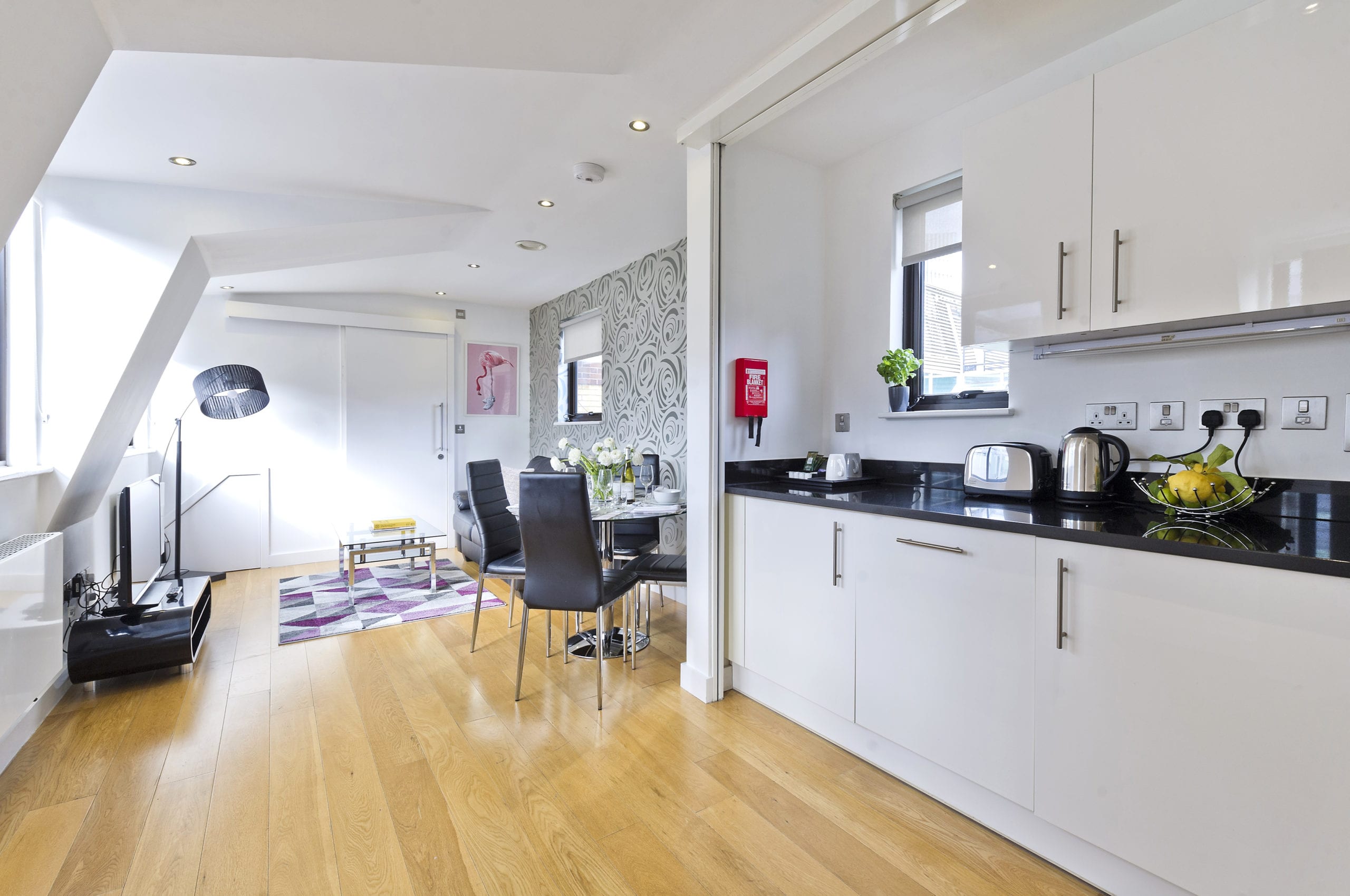 Long kitchen living area with natural light from both sides with the kitchen at one end and a TV and sofa set up